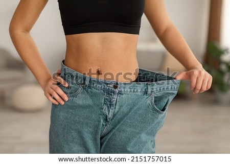 Successful Weight Loss. Unrecognizable Skinny African American Woman Wearing Old Large Jeans After Showing Flat Belly And Great Result After Slimming Standing At Home. Cropped Shot Royalty-Free Stock Photo #2151757015