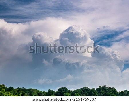 Massive rain cloud, Cumulus congestus, in the blue sky over the treetops Royalty-Free Stock Photo #2151759387