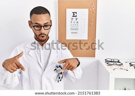 African american optician man standing by eyesight test pointing down with fingers showing advertisement, surprised face and open mouth 