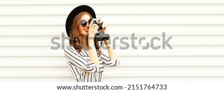 Portrait of happy young woman photographer taking picture on film camera wearing black round hat, striped shirt on white background, banner blank copy space for advertising text