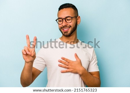 Young hispanic man isolated on blue background taking an oath, putting hand on chest.