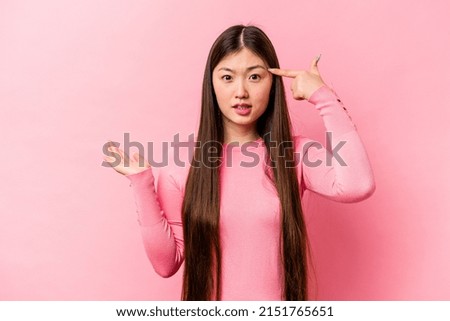 Young Chinese woman isolated on pink background holding and showing a product on hand.