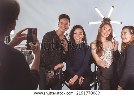Two fashion models or actresses have their selfies taken with their makeup artist and hairstylist.