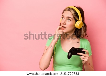 Young caucasian woman playing with a video game controller isolated on pink background relaxed thinking about something looking at a copy space.