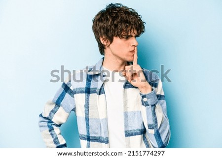 Young caucasian man isolated on blue background keeping a secret or asking for silence.
