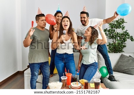 Group of young hispanic friends having birthday party singing song using microphone at home.