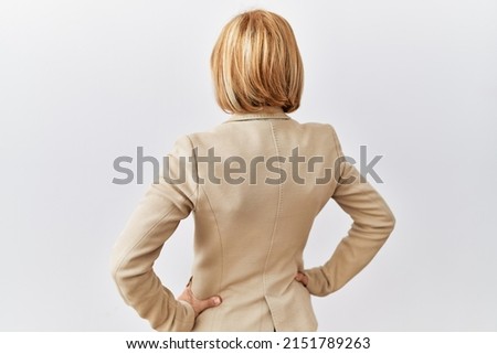 Middle age blonde business woman standing over isolated background standing backwards looking away with arms on body 