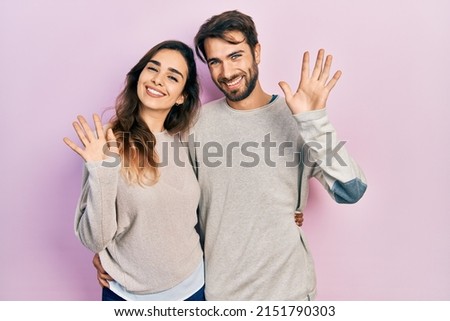Young hispanic couple wearing casual clothes waiving saying hello happy and smiling, friendly welcome gesture  Royalty-Free Stock Photo #2151790303