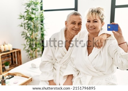 Senior caucasian couple holding credit card sitting on massage table at beauty center.