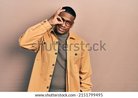 Young black man wearing casual clothes and glasses smiling happy doing ok sign with hand on eye looking through fingers 