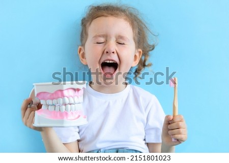 Little cute funny smiling girl holding tooth jaw, toothbrush. Kid training oral hygiene. Child learning brushing, cleaning teeth. Prevention of caries in children. children dentistry. dental care kids Royalty-Free Stock Photo #2151801023