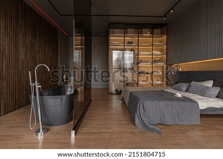 bedroom and freestanding bath behind a glass partition in a chic expensive interior of a luxury home with a dark modern design with wood trim and led light Royalty-Free Stock Photo #2151804715