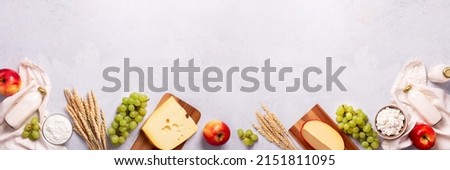 Shavuot flat lay with dairy products, first fruits and wheat on light gray background, web banner. Jewish Shavuot holiday frame with dairy foods and fruits, top view Royalty-Free Stock Photo #2151811095
