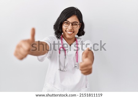 Young hispanic doctor woman wearing stethoscope over isolated background approving doing positive gesture with hand, thumbs up smiling and happy for success. winner gesture. 