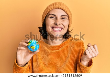 Young brunette woman holding small world ball screaming proud, celebrating victory and success very excited with raised arm  Royalty-Free Stock Photo #2151812609