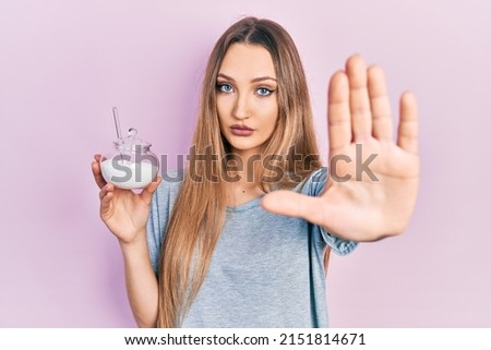 Young blonde girl holding bowl with sugar with open hand doing stop sign with serious and confident expression, defense gesture 