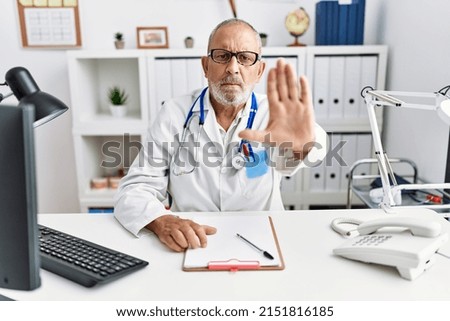 Mature doctor man at the clinic doing stop sing with palm of the hand. warning expression with negative and serious gesture on the face. 