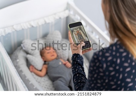 Young mother taking a picture to her newborn baby in the cradle