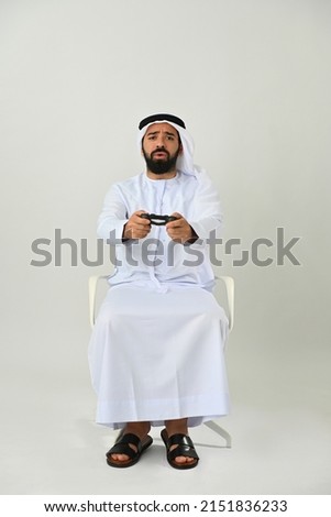 Arab Emirati gamer man playing video game enjoying being happy and excited wearing traditional UAE dress isolated on solid white background