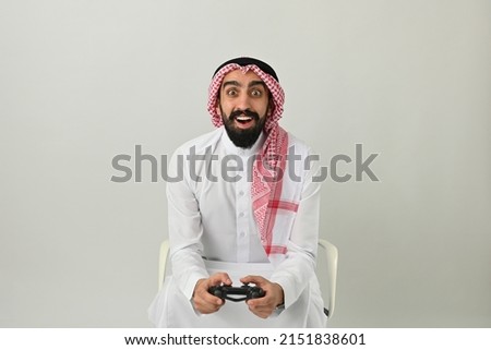 Saudi Arab man gamer enjoying video game excited and happy wearing traditional Saudi Arabia dress isolated on solid white background