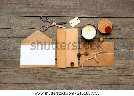 Envelopes with blank card, candle and scissors on wooden background