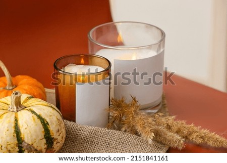 Holders with burning candles and pumpkin on table, closeup