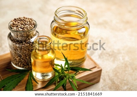 Board with bottles of hemp oil and seeds on light background, closeup Royalty-Free Stock Photo #2151841669
