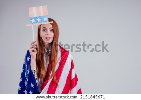 happy young and beautiful redheaded businesswoman wearing Uncle Sam hat with american symbols drawn on cardboard with American flag on white background in studio : independence day usa 4th of july