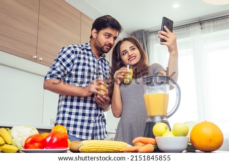 healthy and eco lifestyle.happy indian woman with her husband making smoothie in big kitchen,taking photos portrait on smartphone camera
