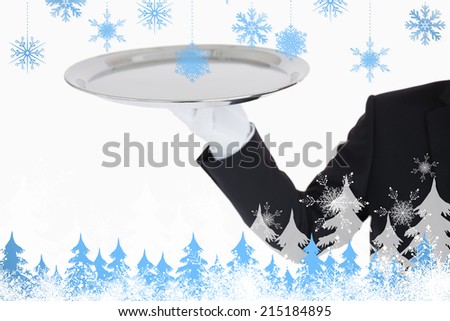 Hand with white gloves holding a silver tray against snowflakes and fir trees