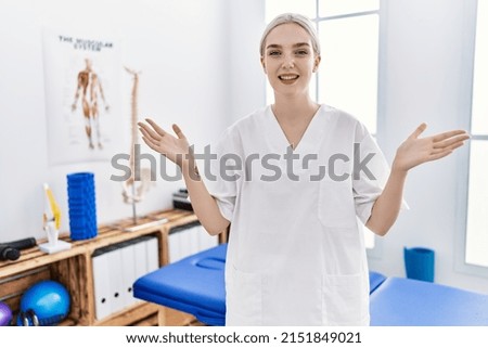 Young caucasian woman working at pain recovery clinic smiling cheerful offering hands giving assistance and acceptance. 