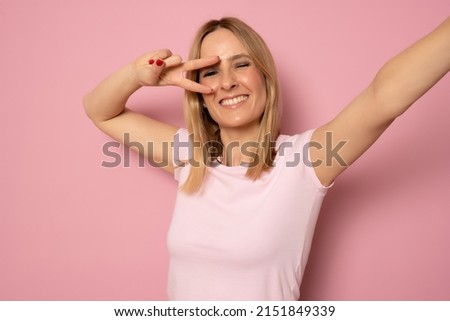 White brunette happy young woman showing peace sign while taking selfie photo isolated over pink background