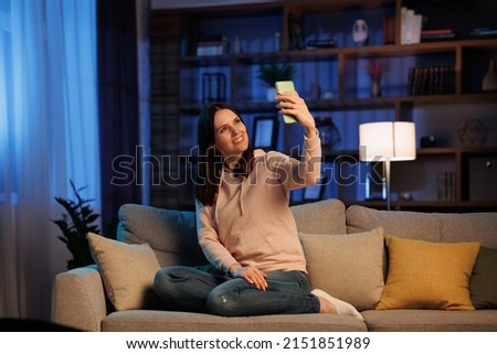 Portrait of a beautiful smiling woman making selfie photo on smartphone. Home leisure in the evening, cinematic lighting