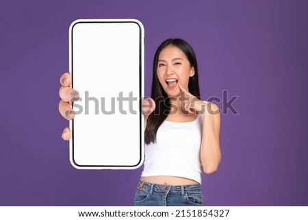 Beautiful Asian brunette woman cute girl in white tank top ,Excited surprised girl showing big smart phone with blank screen , white screen isolated purple background , Mock Up Image Royalty-Free Stock Photo #2151854327