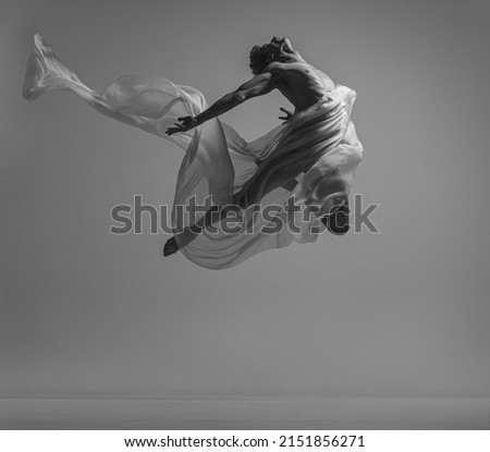 Freedom. Black and white portrait of graceful muscled male ballet dancer dancing with fabric, cloth isolated on grey background. Grace, art, beauty, contemp dance concept. Weightless, flexible actor