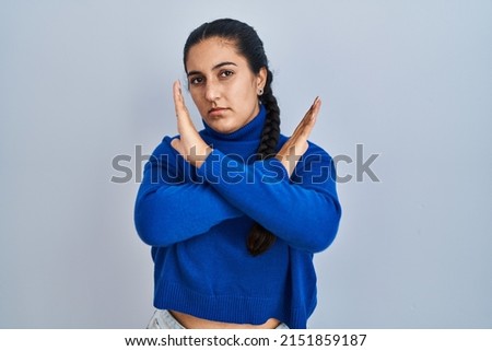 Young hispanic woman standing over isolated background rejection expression crossing arms doing negative sign, angry face 