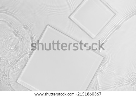 Two empty clear white square podiums on transparent calm water texture with splashes and waves in sunlight. Abstract nature background for product presentation. Flat lay cosmetic mockup, copy space. Royalty-Free Stock Photo #2151860367