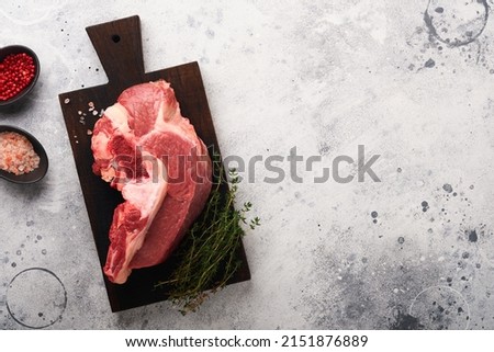 Raw beef meat. Rough piece of meat on bone for roast or soup with salt, pepper, thyme and rosemary on old grey concrete table background. Entrecote. Raw cowboy steak. Top view.