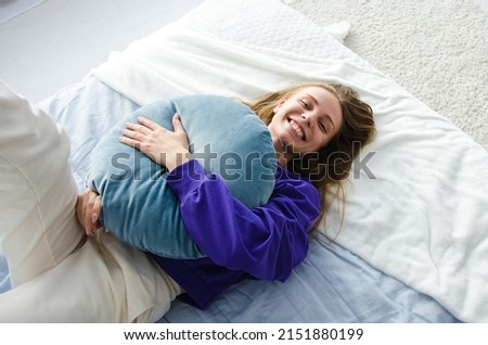 the girl lies on the bed and hugs the pillow in a purple sweater and smiles at the camera. the concept of a fun morning Royalty-Free Stock Photo #2151880199