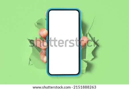 Cellular App. Male hand holding smartphone with white empty screen showing device close up to camera breaking through torn green paper sheet. Gadget display with free copy space, mock up. Great Offer