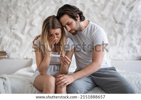 Upset young woman with negative pregnancy test crying on bed, loving husband supporting her at home. Medical disorders and problems in childbearing, infertility concept Royalty-Free Stock Photo #2151888657