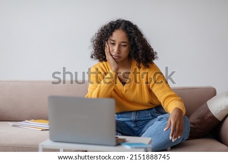 Millennial black woman feeling bored near laptop during online business meeting at home office, copy space. Tired young African American female overworking on freelance job in living room
