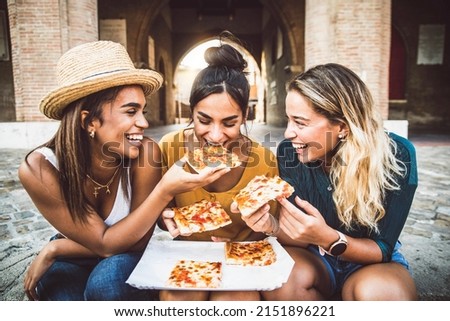 Three young female friends eating pizza sitting outside - Happy women enjoying street food in the city - Italian food culture and european holidays concept Royalty-Free Stock Photo #2151896221