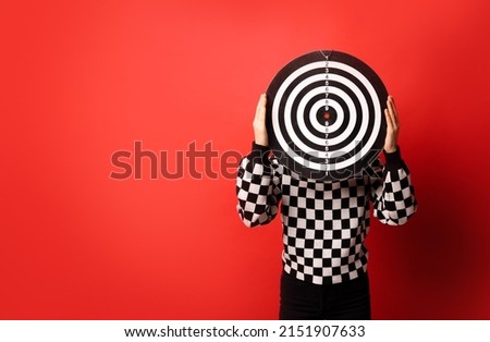 A human holding target in front of her head on red background. Targeting in psychology or in business concept.