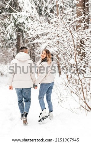 Winter love story. A young couple is holding hands and running through the forest. Snow forest. Snowfall. Bright and positive emotions. The couple looks at each other. Kiss of a young couple