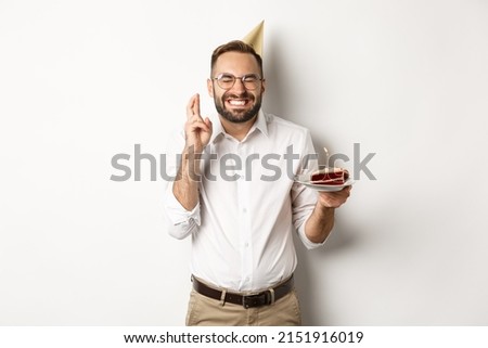 Holidays and celebration. Happy man making wish on birthday cake, cross fingers and smiling excited, having b-day party, white background