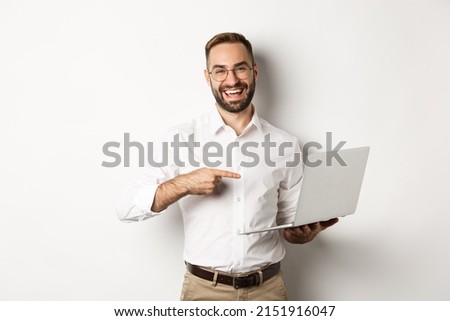 Business. Handsome manager in glasses working on laptop, pointing at computer and smiling pleased, standing over white background