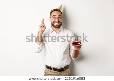 Holidays and celebration. Happy man having birthday party, making wish on b-day cake and cross fingers for good luck, standing against white background