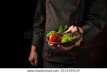 Grilled and sliced beef steak with grilled vegetables served on plate on black background presentation in chef hands. Grande cuisine.