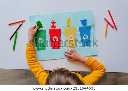 Little girl playing with poster of garbage containers for sorting at kindergarten or primary school. Recycling education concept. Royalty-Free Stock Photo #2151944633
